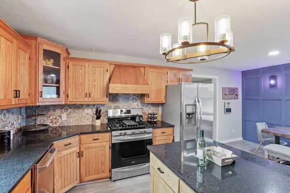 A kitchen with wooden cabinets, a stainless steel refrigerator, a gas stove, and a modern chandelier.