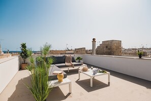Een terras op het dak met een bank, salontafel en plantenpotten.