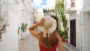 A narrow street with white buildings, a woman in a red dress, and potted plants. - Le Terrazze di Don Nino (Polignano a Mare)