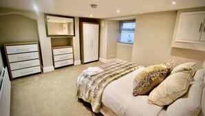 A bedroom with a bed, a dresser, a wardrobe, a mirror, and a window. - Mill House Townhouse (Newmarket)