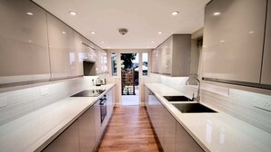 A modern kitchen with two sinks, wooden flooring, and a view of the outdoors. - Mill House Townhouse (Newmarket)