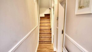 A hallway with wooden flooring, white walls, and a white radiator. - Mill House Townhouse (Newmarket)
