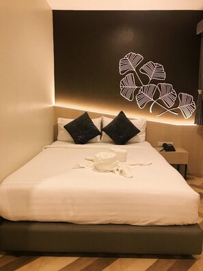 A neatly made bed with white linens and black pillows, a bedside table with a phone, and a wall with a leaf-like light fixture. - SJ Miracle Hotel (Hat Yai)