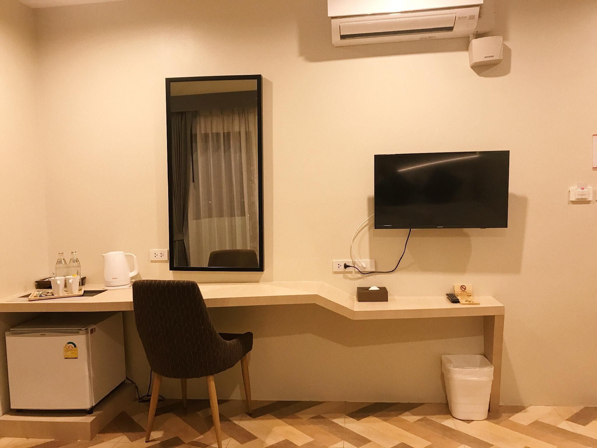 Habitación de hotel con escritorio, silla, televisión, aire acondicionado, mini refrigerador y un cesto de basura.