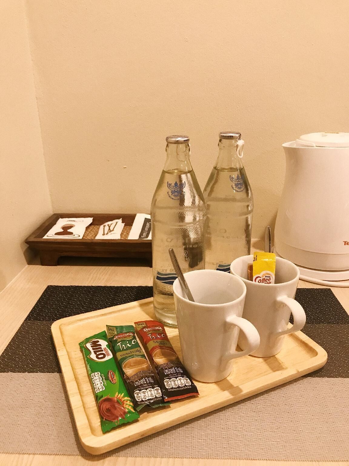 Una bandeja con una taza, dos botellas, una cafetera y algunos bocadillos.