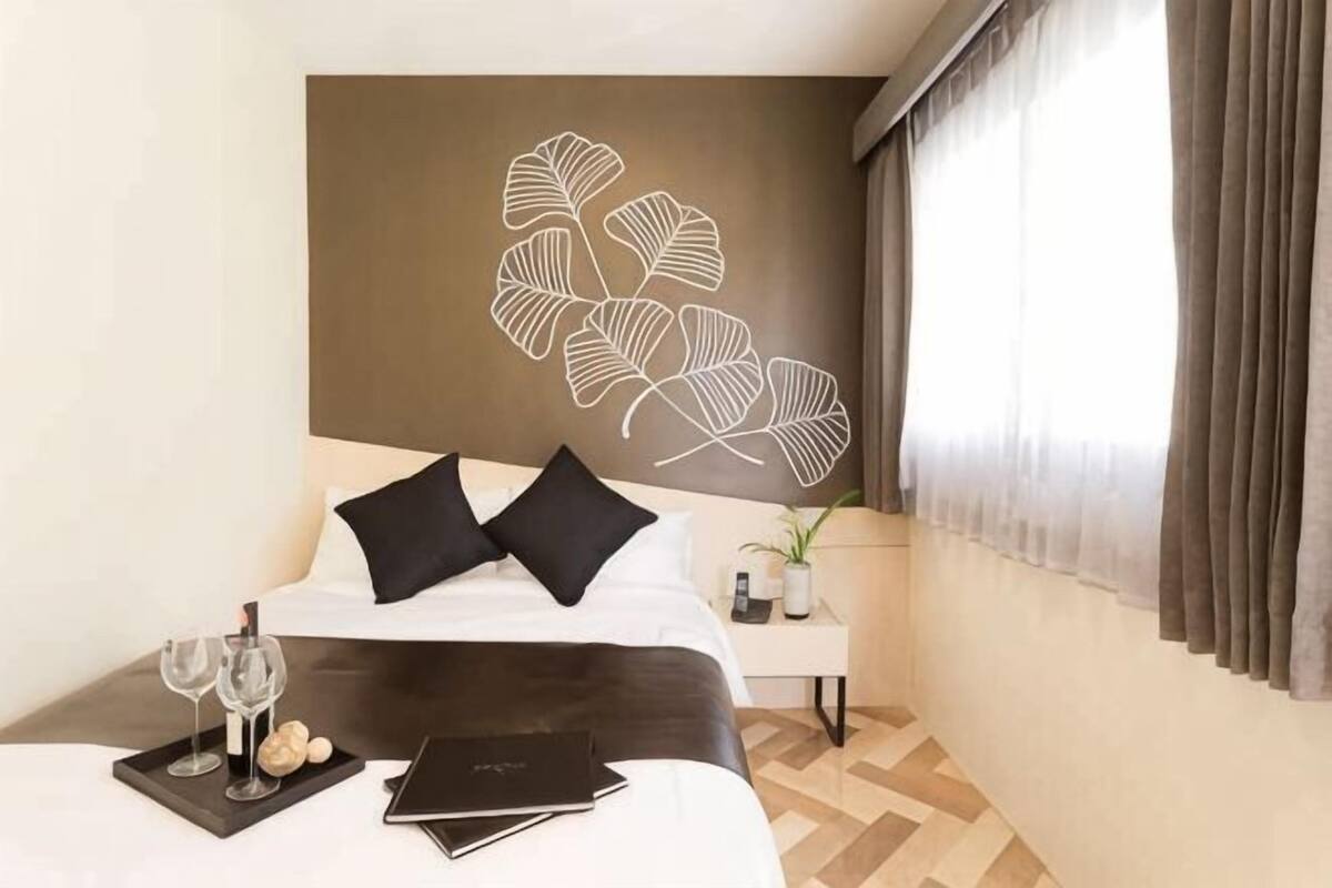 Une chambre d’hôtel avec un lit, une table de chevet ornée d’une plante et une fenêtre avec des rideaux.