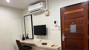 A hotel room with a wooden door, a desk with a computer, a mirror, and a trash bin. - SJ Miracle Hotel (Hat Yai)