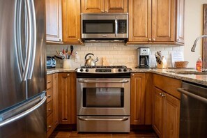 A kitchen with stainless steel appliances, wooden cabinets, and a tiled backsplash.