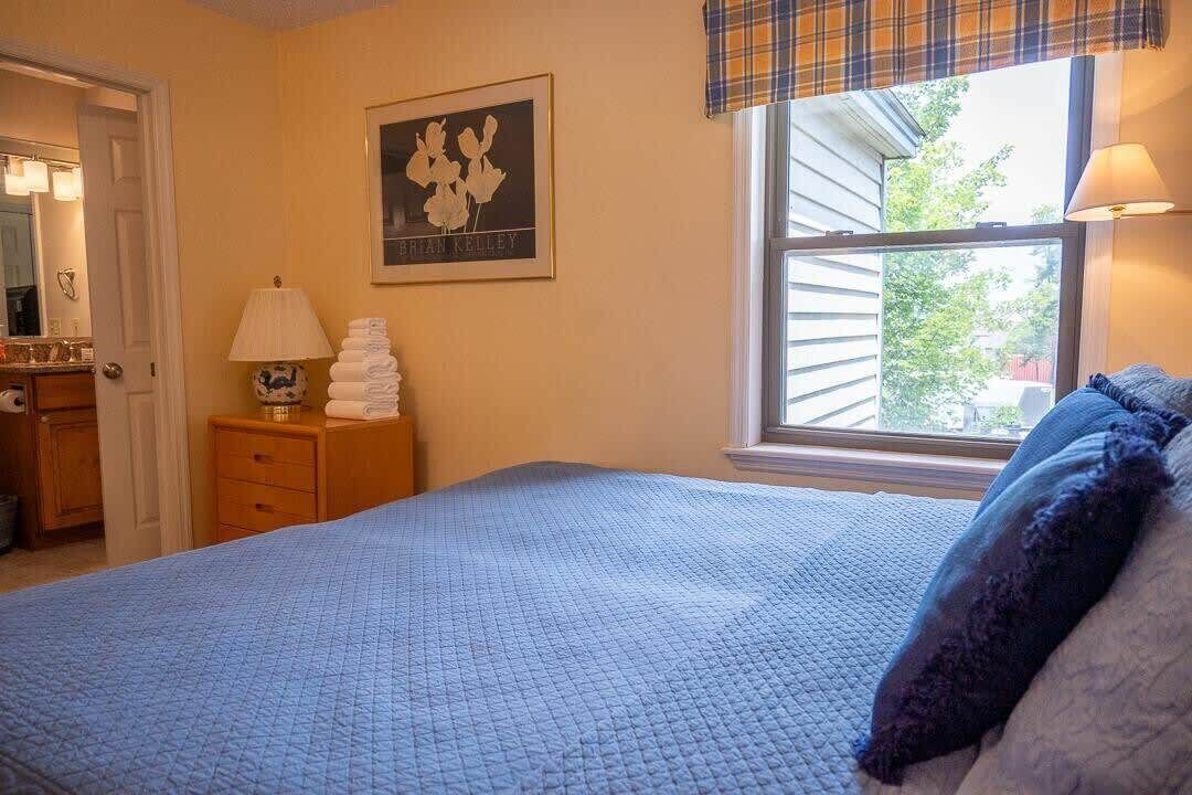 Ein Schlafzimmer mit Bett, Fenster mit Blick, einem gerahmten Bild an der Wand und einer Lampe auf dem Nachttisch.
