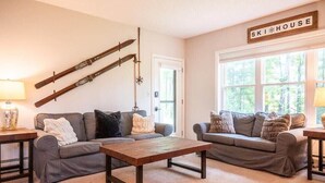 A cozy living room with two grey sofas, a wooden coffee table, and skis mounted on the wall. - 3BR Okemo Escape: Premier Condo Steps to Trail (Ludlow)