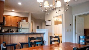A kitchen with wooden cabinets, a refrigerator, and a dining area with a wooden table and chairs. - 3BR Okemo Escape: Premier Condo Steps to Trail (Ludlow)