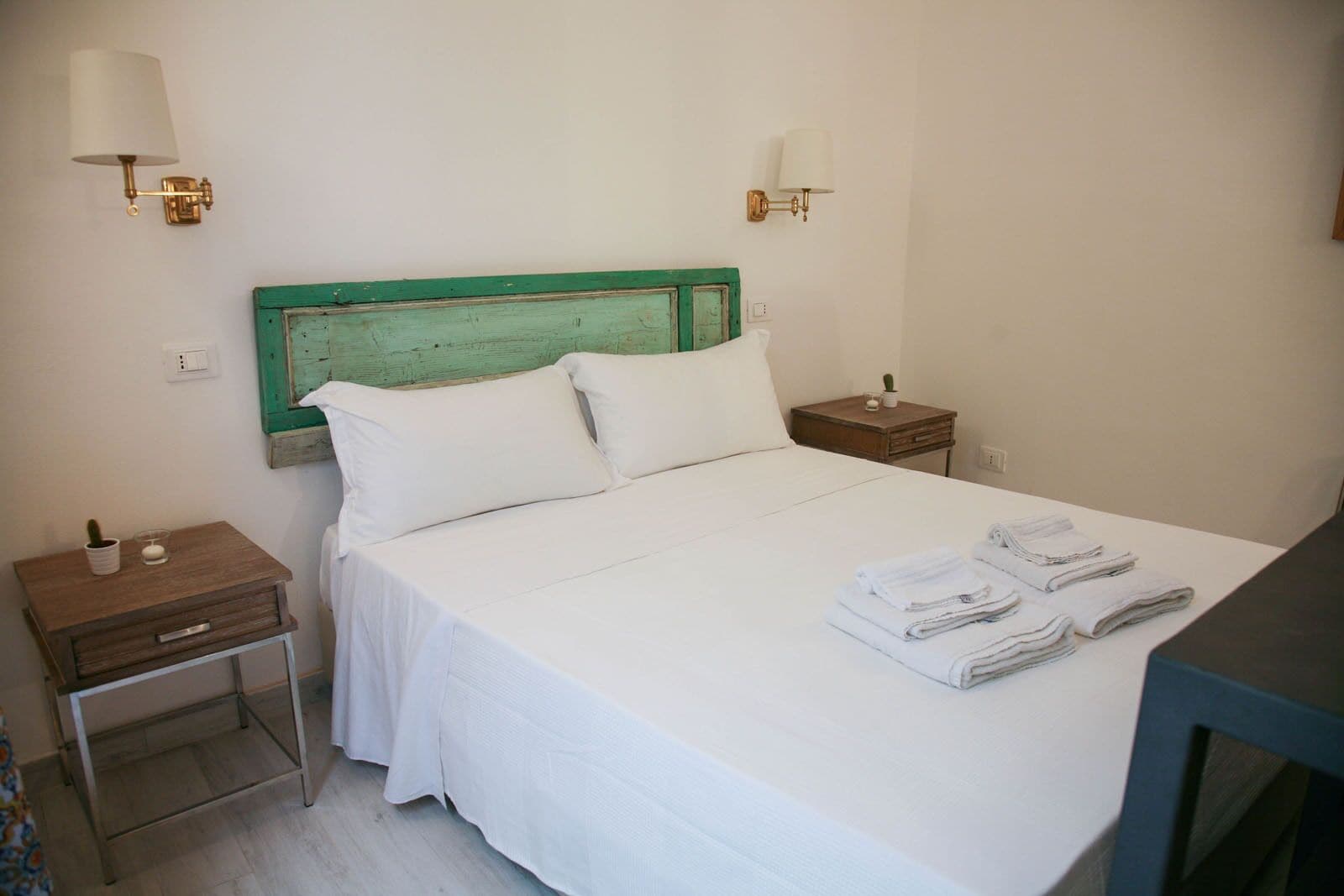 A neatly made bed with white linens, two bedside tables, and a green-painted headboard.