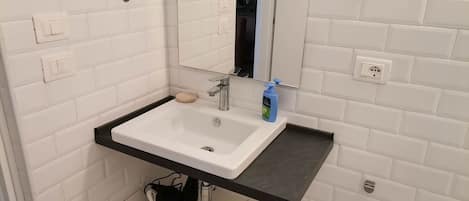 A bathroom with a white sink, a mirror, a black countertop, and a white tiled wall.