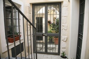 A narrow entrance with a metal gate, potted plants, and a view of a courtyard with a building in the background. - Lanterne Magiche Dependance (Syracuse)