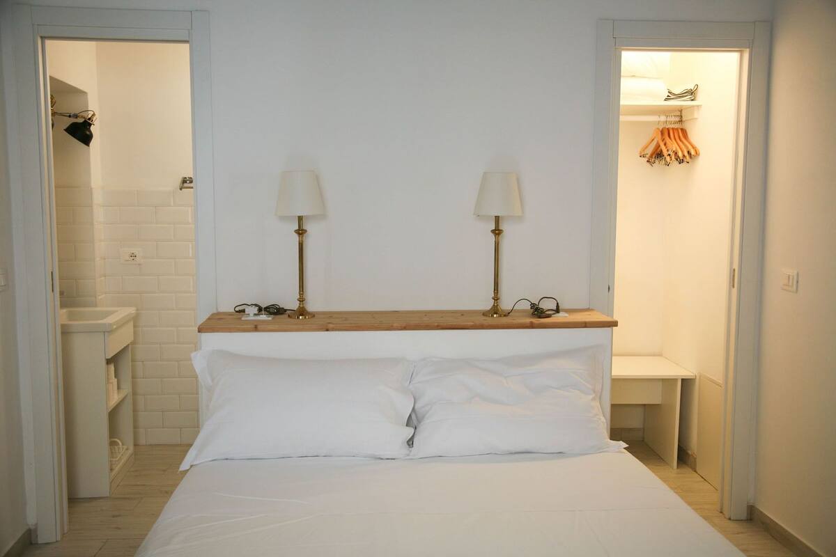 A bedroom with a wooden headboard, two bedside lamps, a white bed, and a wooden nightstand with a lamp.