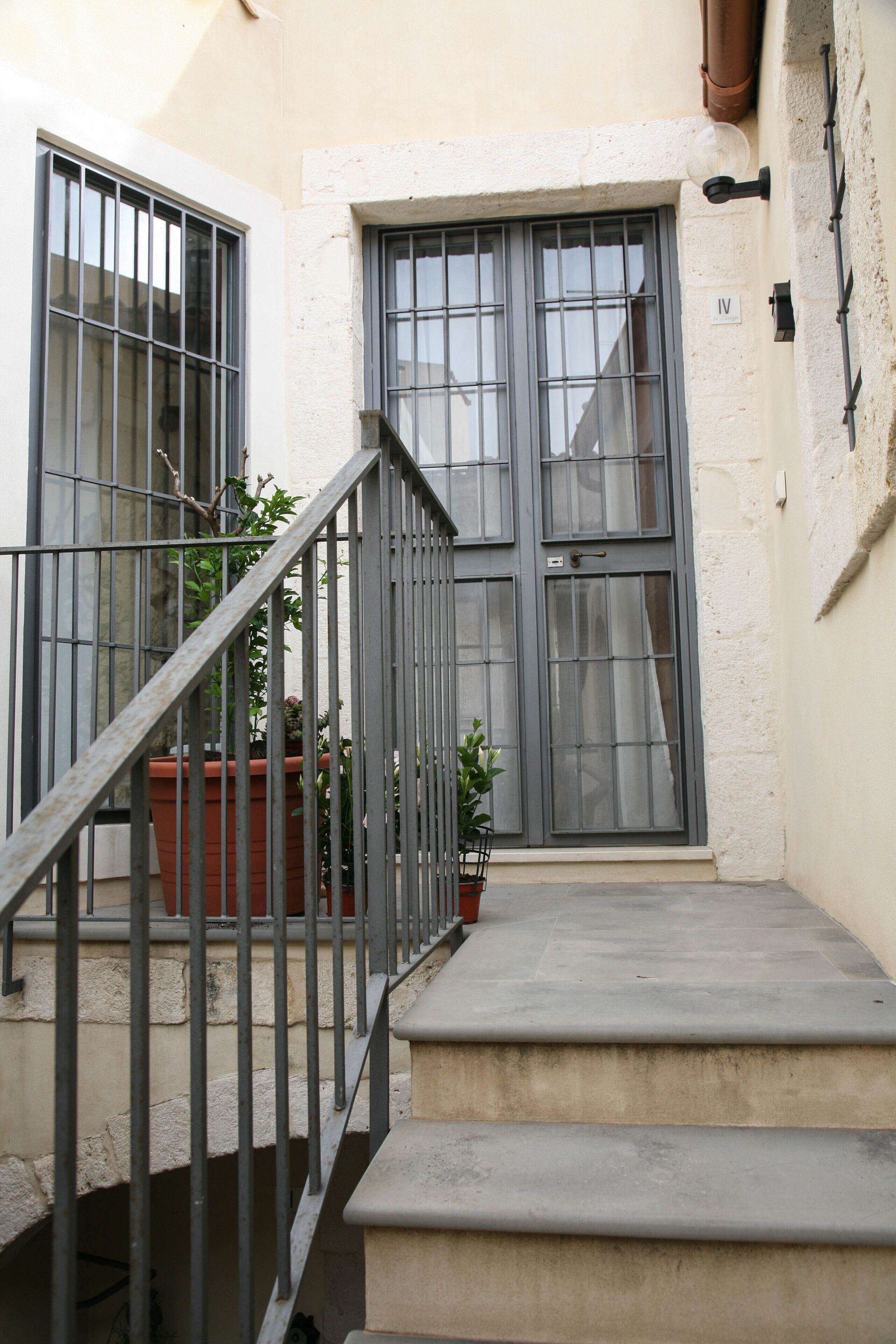 A staircase leading to a door with barred windows, a potted plant, and a wall-mounted light fixture.