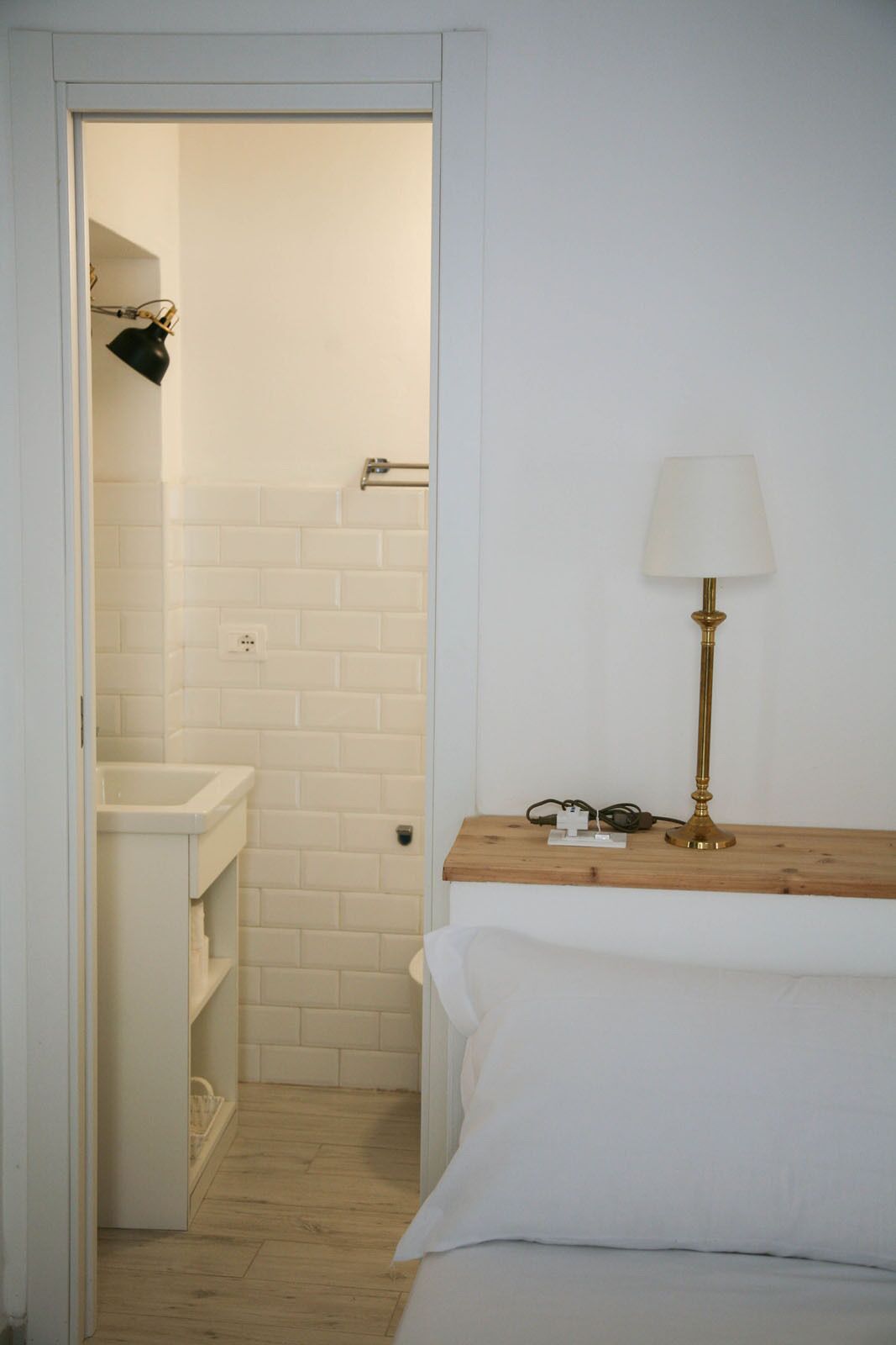 A bathroom with a white sink, a towel rack, and a wooden nightstand with a lamp.