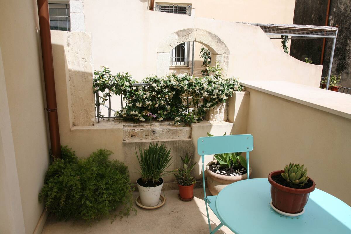 A small balcony with potted plants, a chair, and a table.