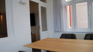 Une pièce avec une table en bois et deux chaises, un téléviseur dans un coin et une fenêtre avec des rideaux.