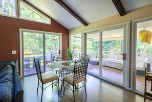 A spacious living area with a glass door leading to an outdoor deck, a dining table with chairs, and a sofa.