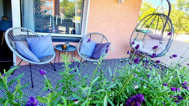 Een balkon met rieten stoelen, een hangstoel en een vloer met een patroon.