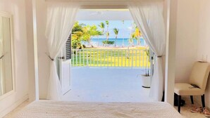 Quarto com uma cama grande, uma cadeira e vista para uma praia com palmeiras.