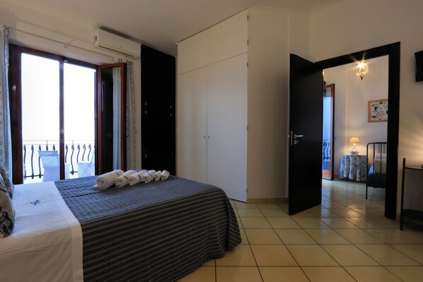 Una habitación de hotel con una cama, un armario, un balcón y una puerta que da a otra habitación.