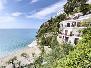 Un hotel frente al mar con balcones que dan a la playa y abundante vegetación.