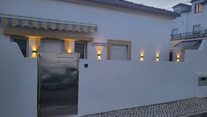 A building with a white facade, a metal gate, and a cobblestone street. - Cheirinho a Mar House (Nazaré)