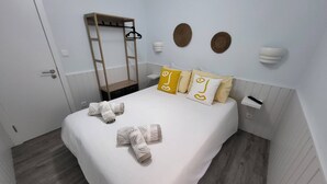 A neatly made bed with towels, a wooden ladder, and wall-mounted light fixtures. - Cheirinho a Mar House (Nazaré)