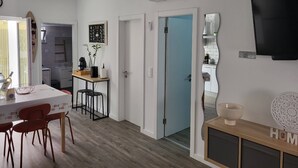 A modern kitchen with white cabinets, a dining area with a table and chairs, and a TV mounted on the wall. - Cheirinho a Mar House (Nazaré)