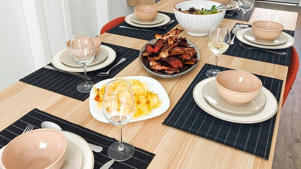 A dining table set with plates, bowls, and glasses, with a television mounted on the wall above. - Cheirinho a Mar House (Nazaré)