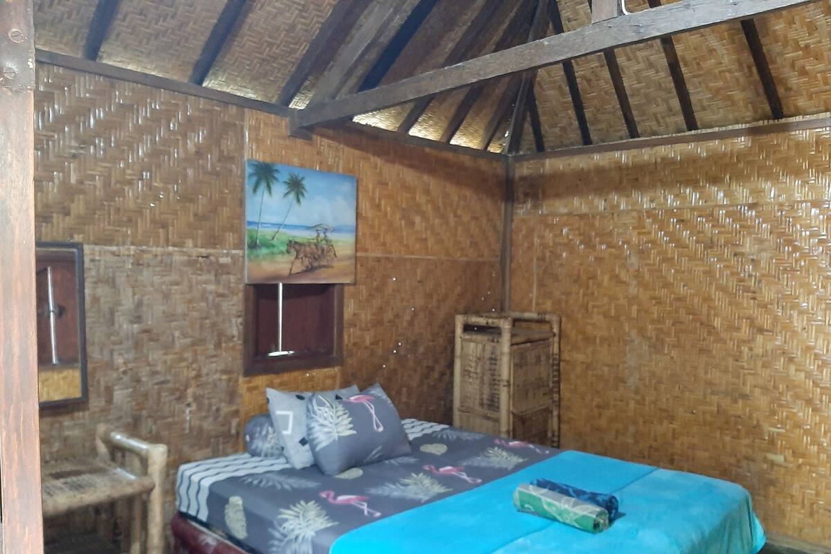 A room with a bed, a chair, a painting on the wall, and a wooden crate.
