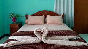 A neatly made bed with a heart-shaped towel arrangement, a wooden headboard, and a teal wall with floral artwork. - New Taman Sari Homestay (Pemenang)