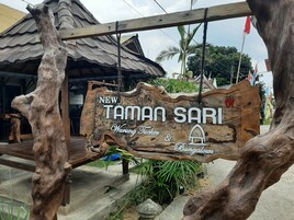 Un letrero de madera con el texto 'NEW TAMAN SARI Warung Tuber & Cingalows' que indica un lugar o establecimiento.