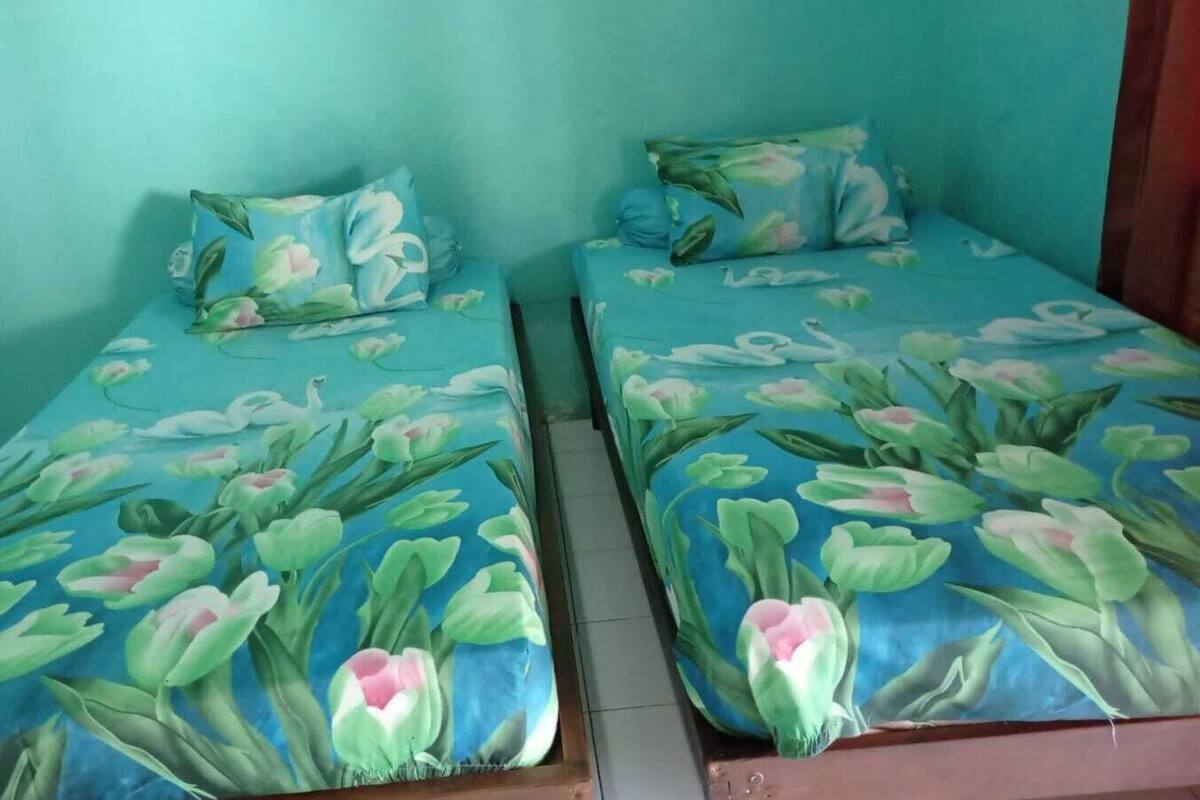 Two twin beds with floral bedding, a wooden headboard, and a teal wall.