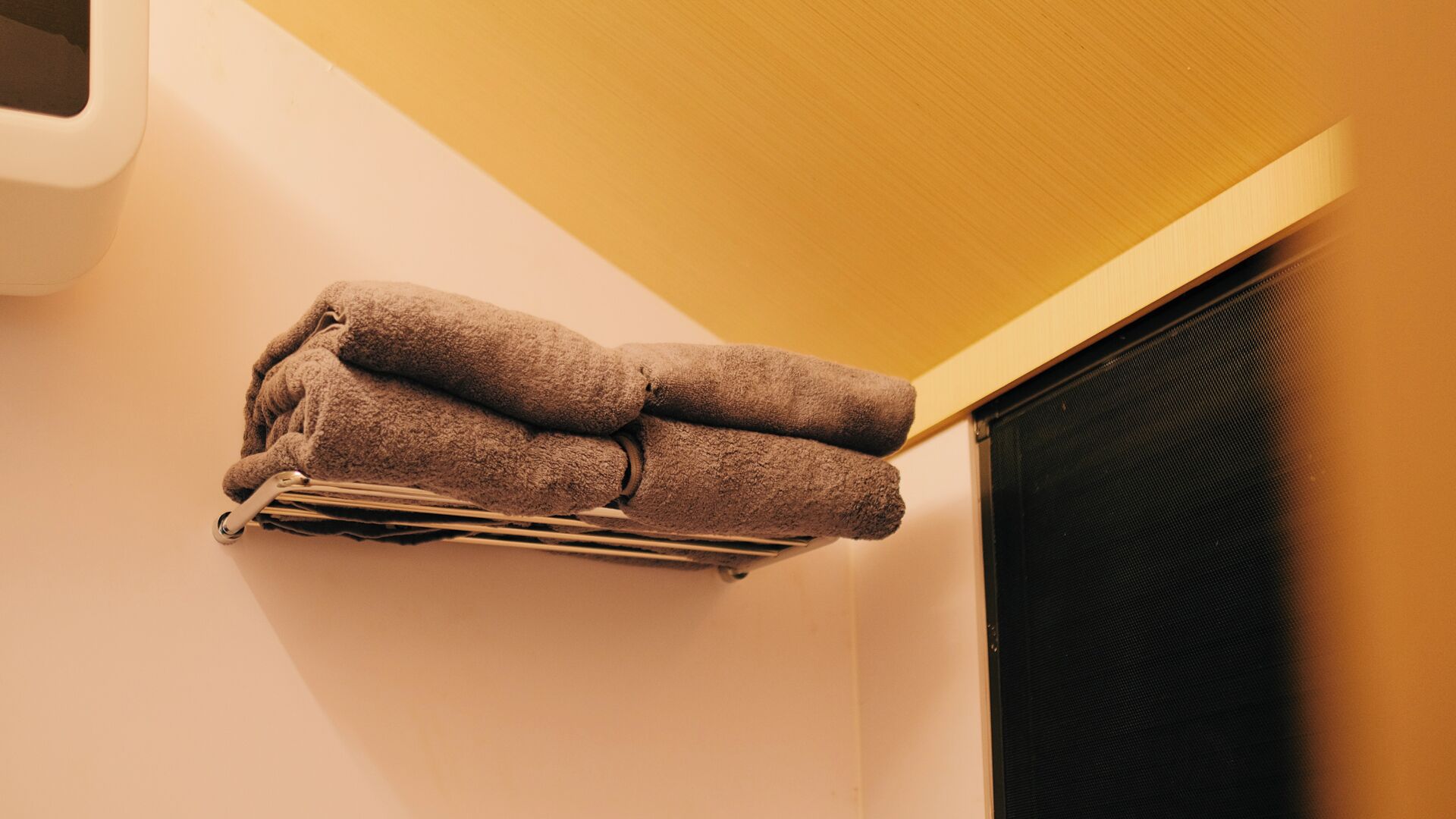A corner of a room with a towel rack holding three folded towels.