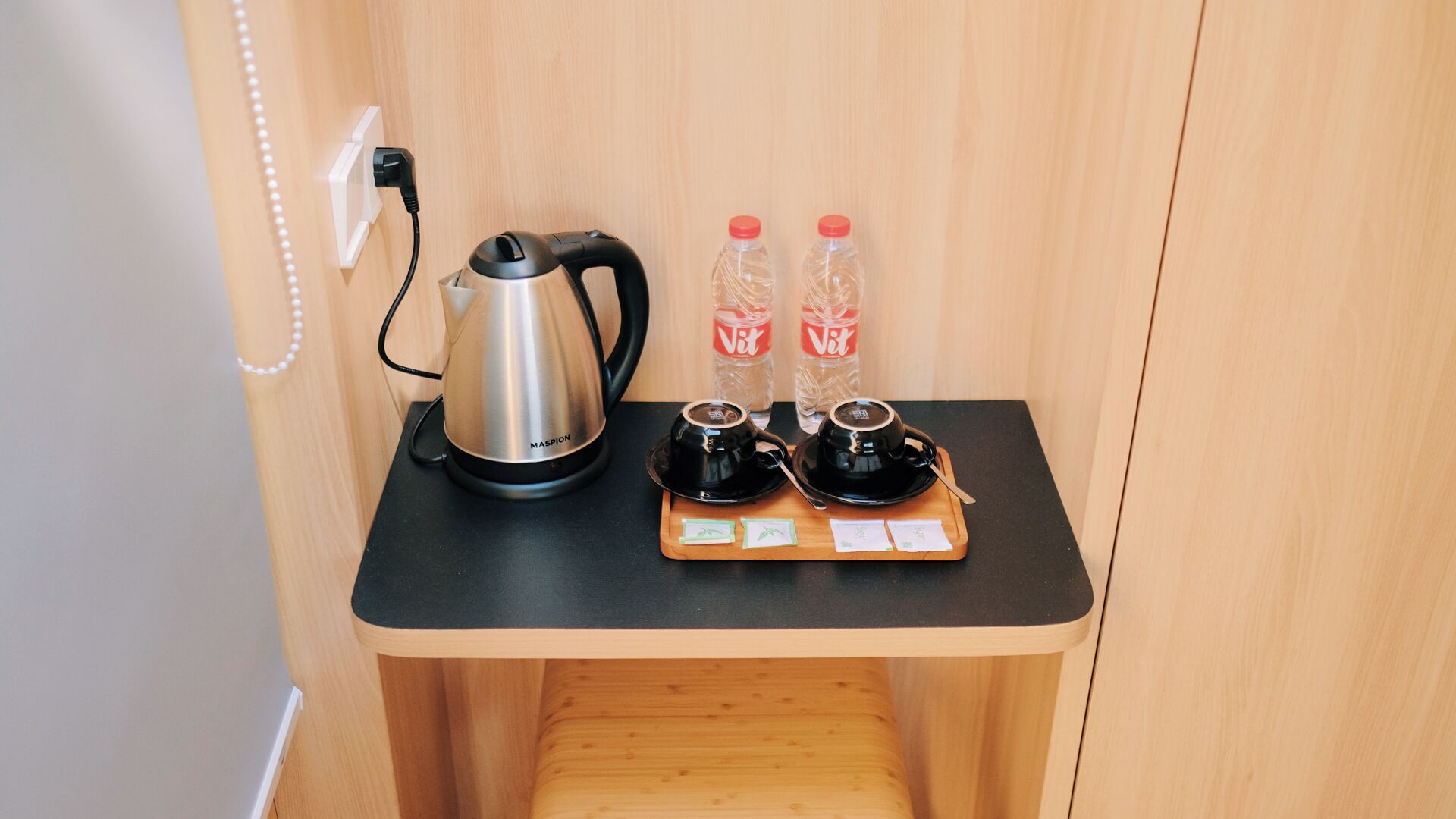 A compact kitchenette with a coffee maker, two cups, and two bottles of water on a wooden counter.