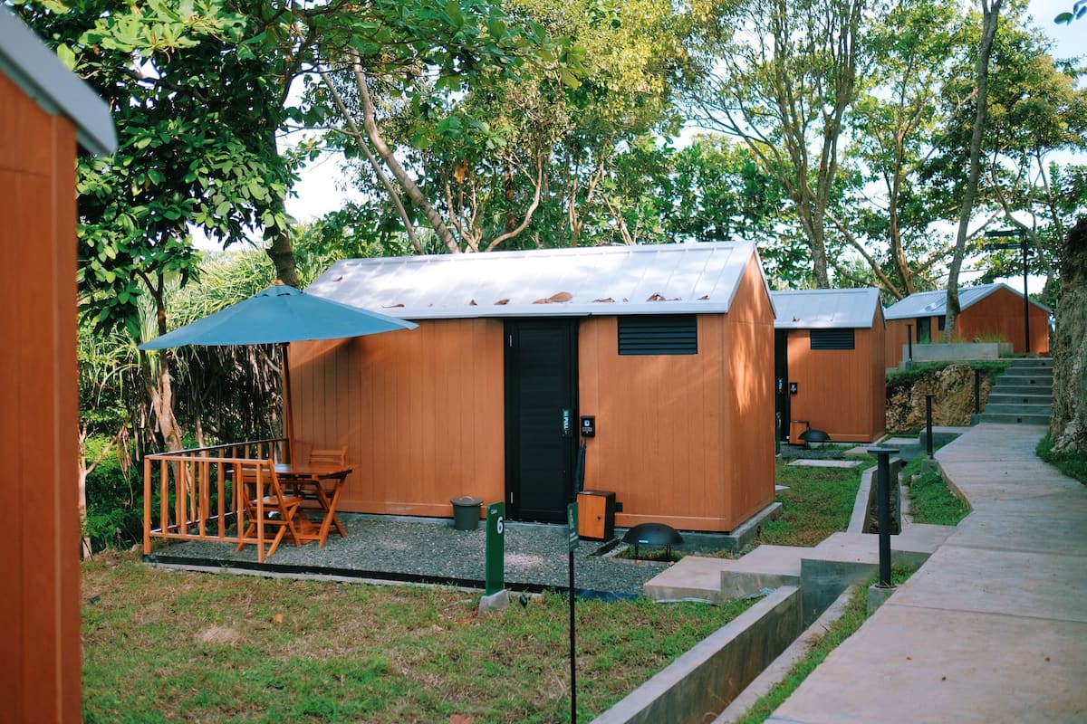 Uma fileira de cabanas de madeira com um caminho de cascalho que as leva, cercada por vegetação.