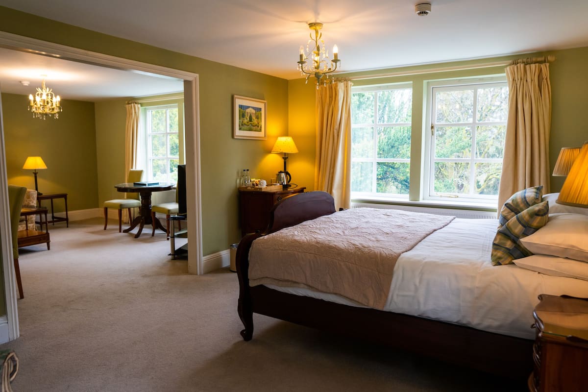 Un dormitorio con una cama grande, un escritorio y una silla. Se ve una ventana con cortinas y un candelabro.