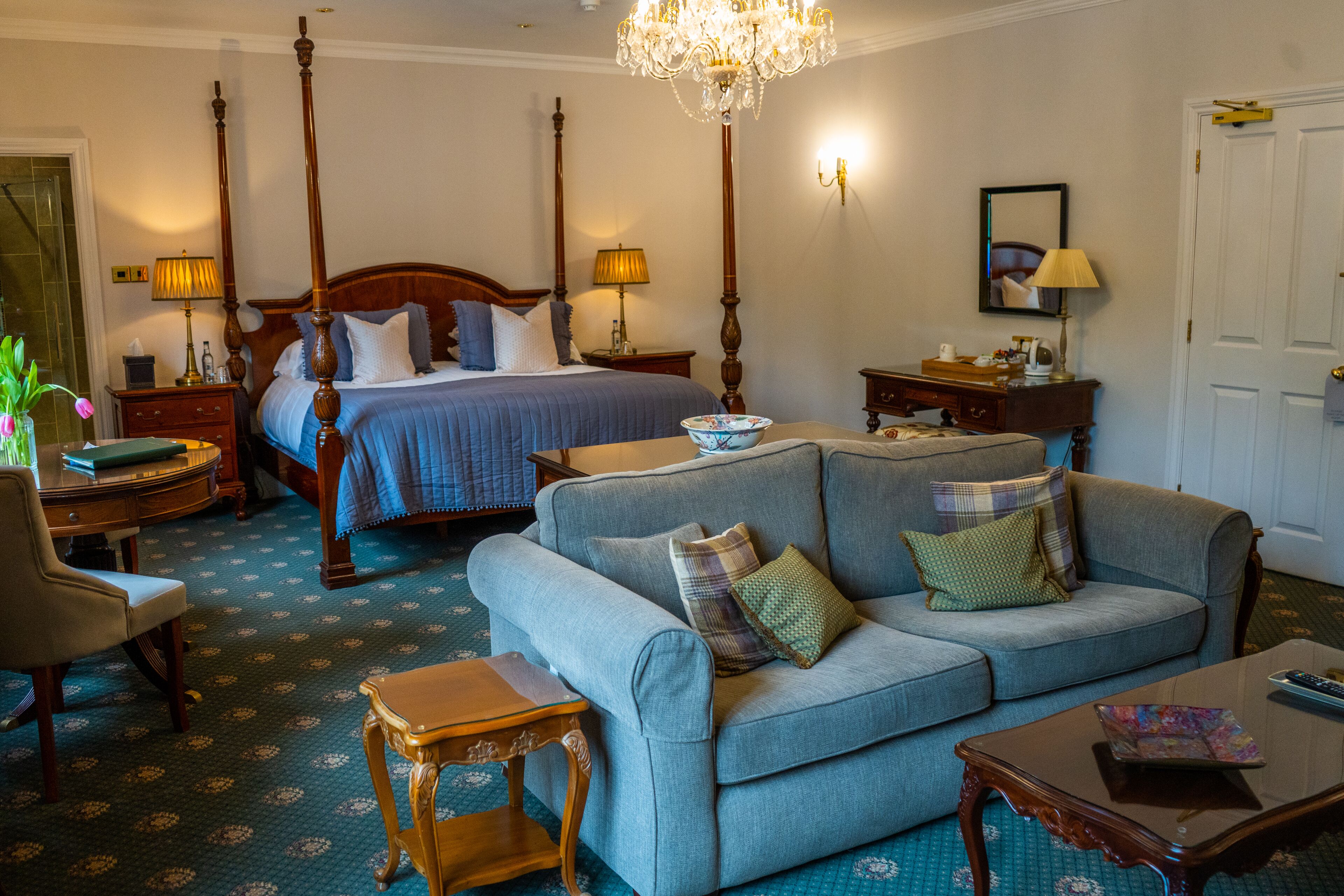 A hotel room with a four-poster bed, a sofa, a small table, and a chair.