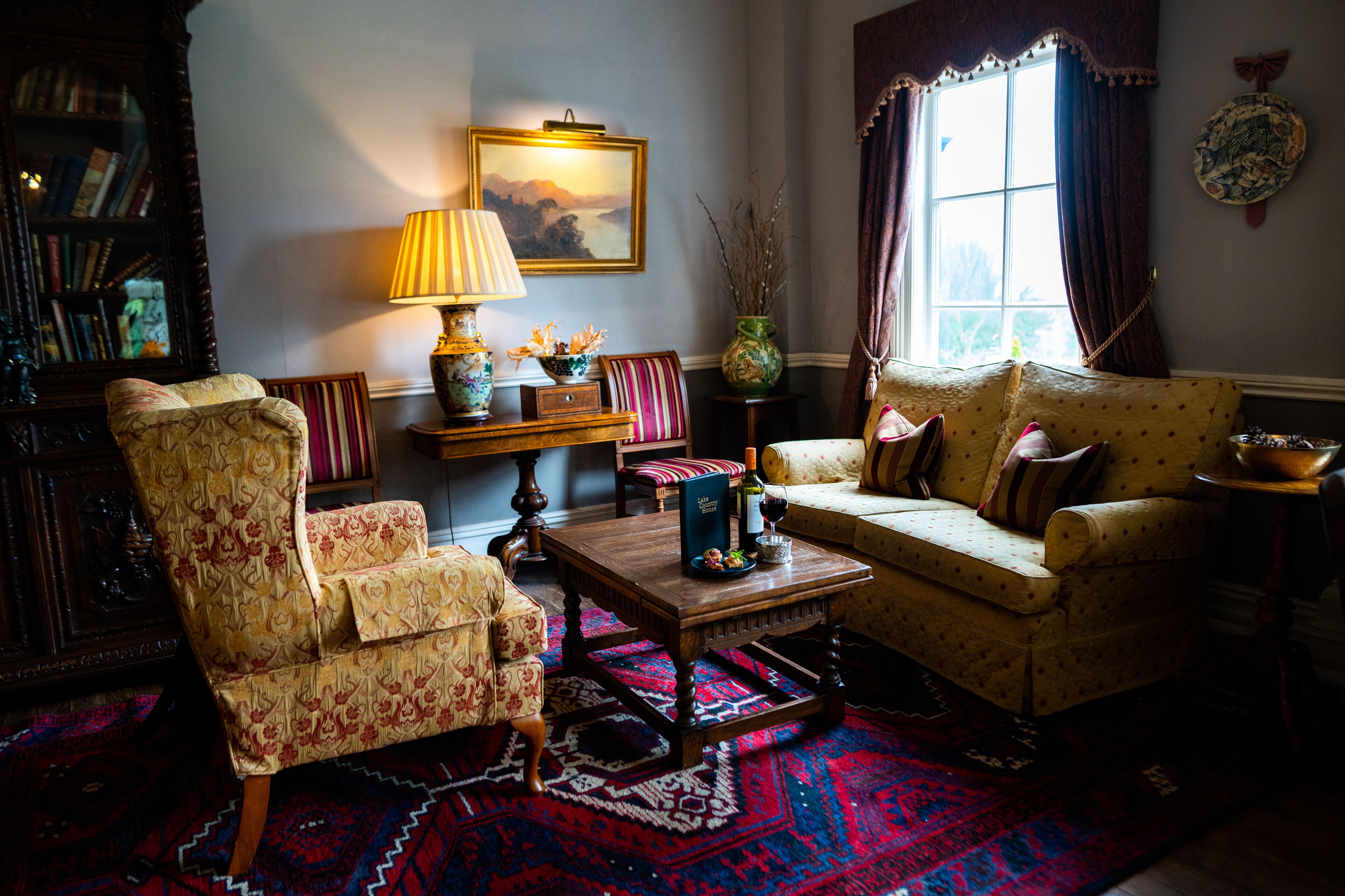 A cozy living room with a patterned armchair, a sofa with cushions, a wooden coffee table, and a bookshelf.