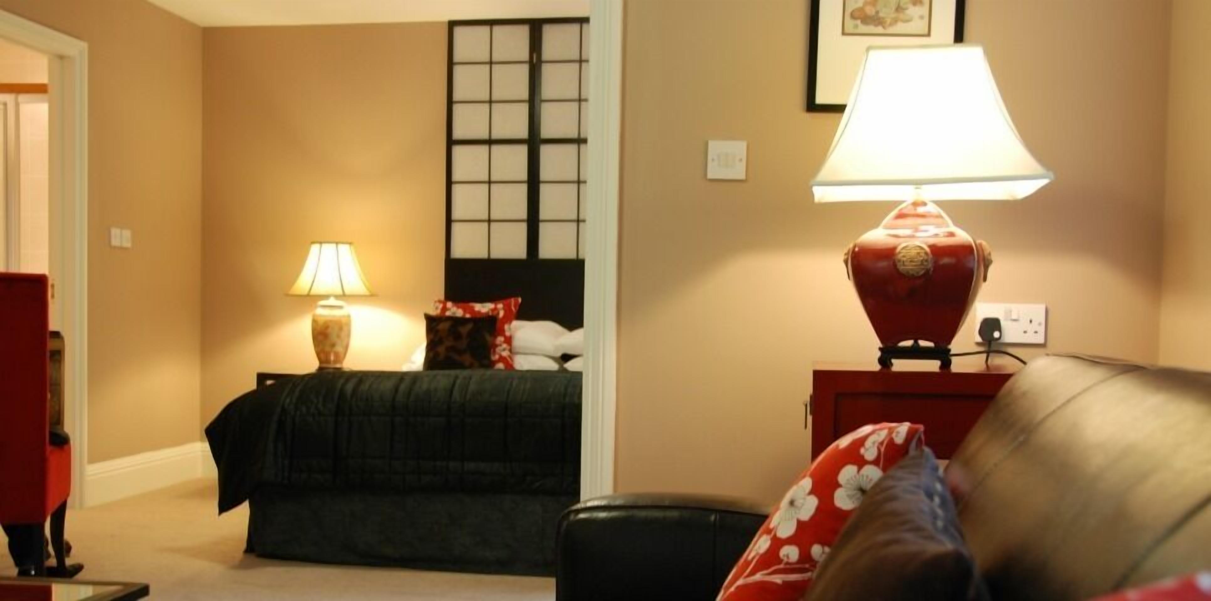 A hotel room with a bed, a nightstand with a lamp, a window with a view, and a door.