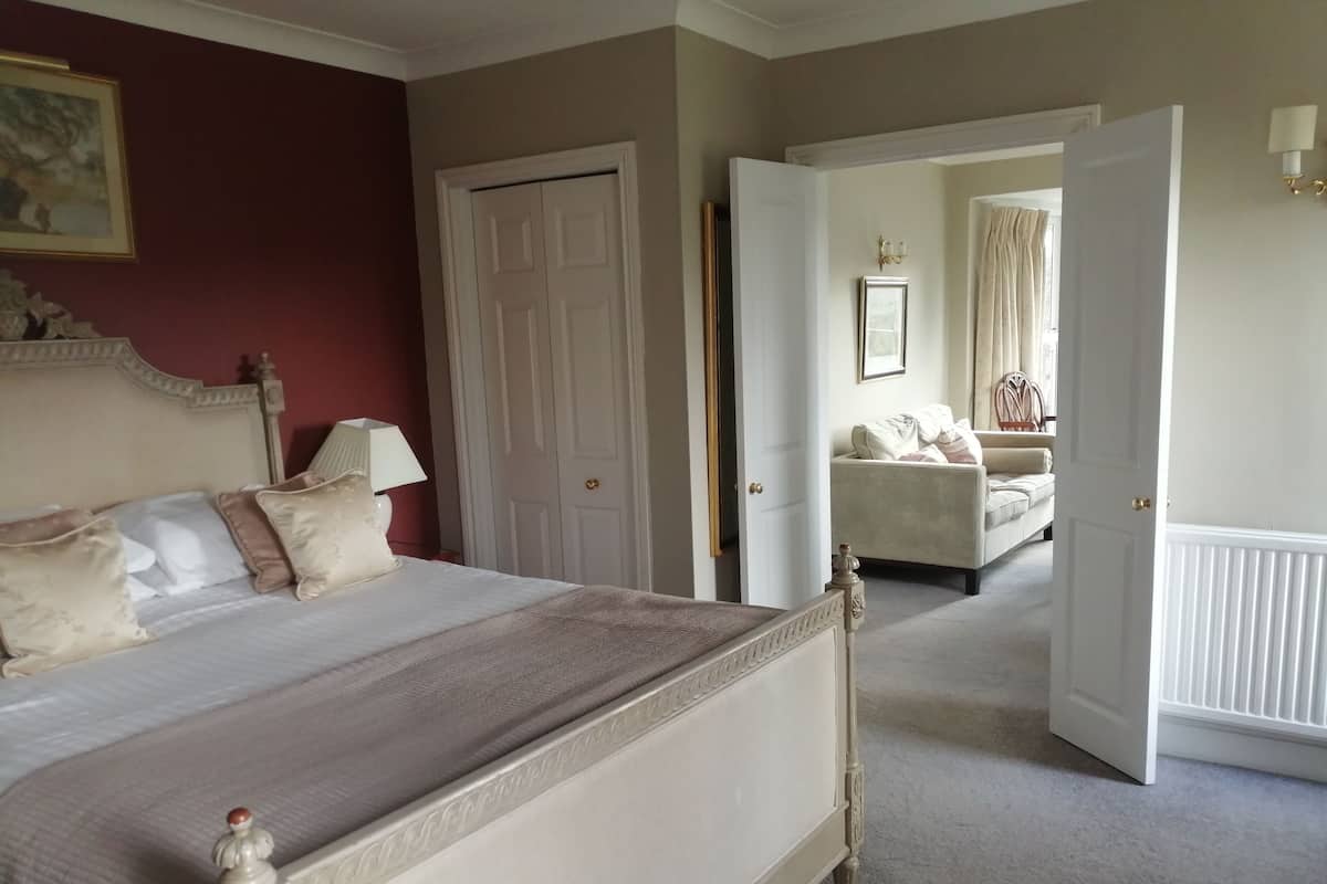 Un dormitorio con una cama grande, una puerta que da a otra habitación y vistas a una sala de estar con sofá y cortinas.