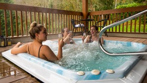 Un jacuzzi con tres personas, rodeado por una terraza de madera y follaje.