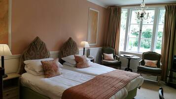 A double bed with a green upholstered headboard, two bedside lamps, and a window with curtains.