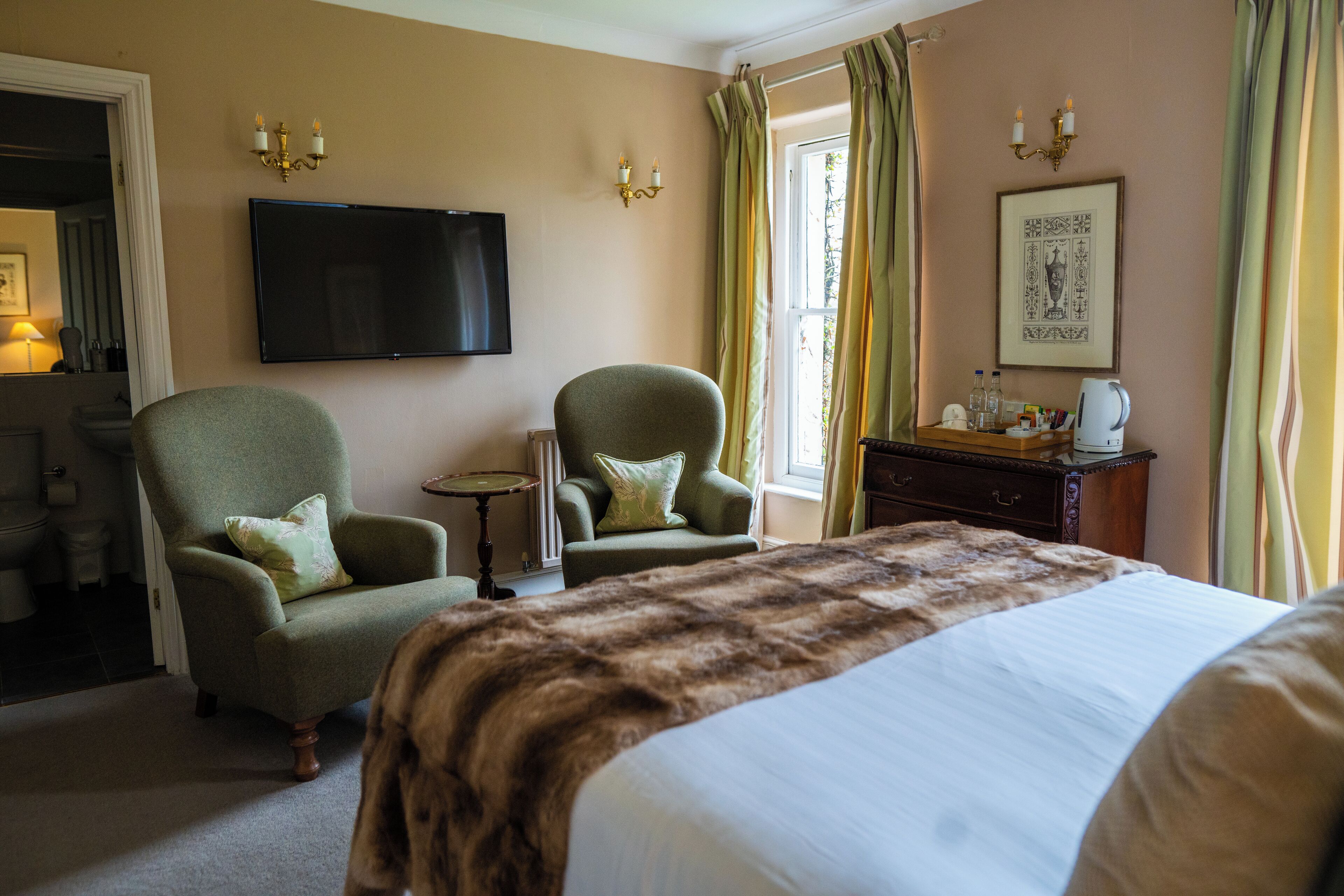 Habitación de hotel con una cama grande, dos sillones, un televisor, una mesita y una ventana con cortinas.