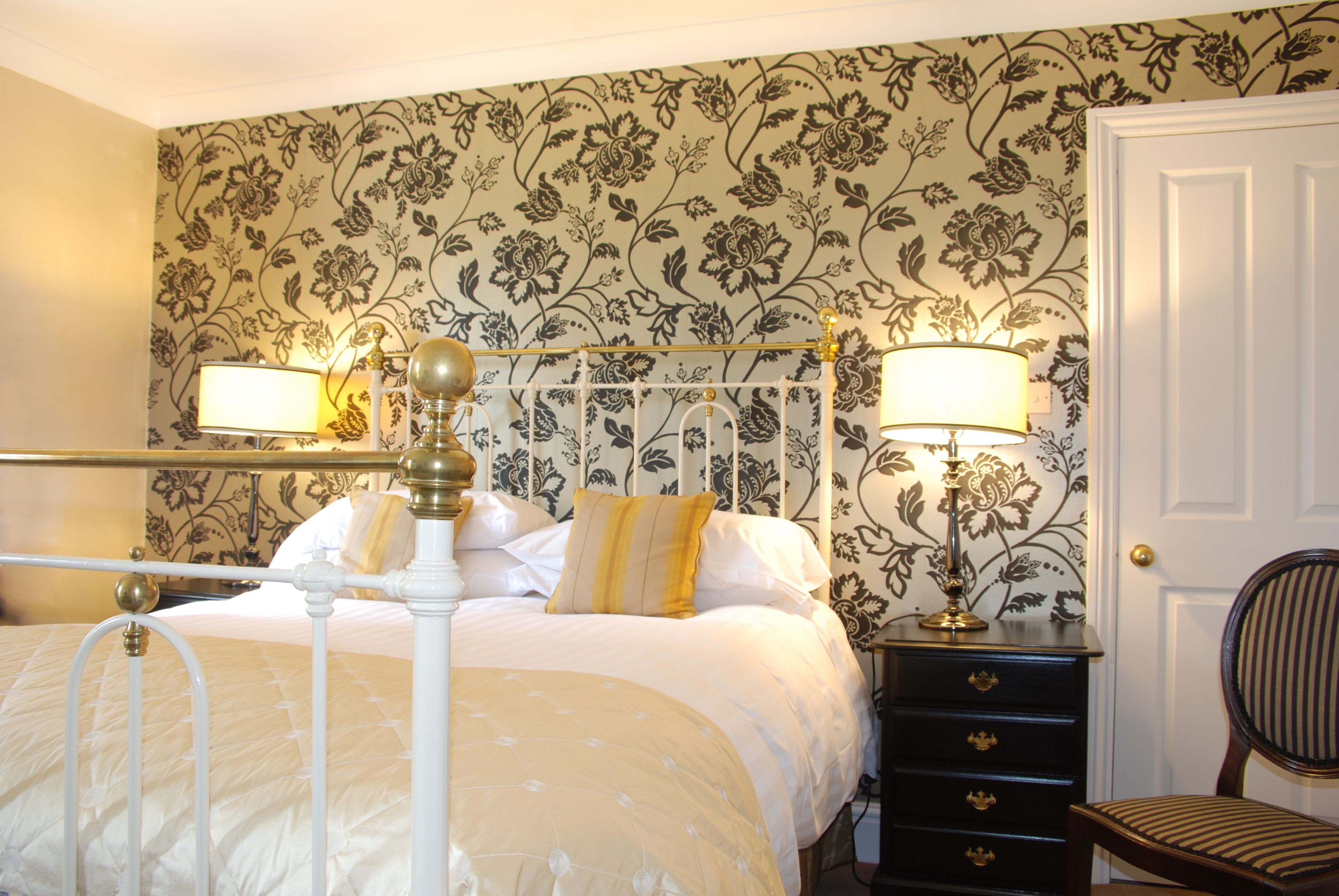 A neatly made bed with a headboard, a bedside table with a lamp, and a chair.