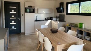 A modern kitchen with a dining area, featuring a wooden table, white chairs, and a view of greenery through a window. - Jolie Dépendance Avec sa Très Belle vue mer (Pietrosella)