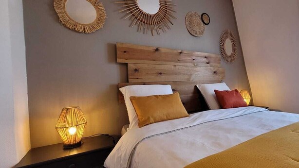 Ein Schlafzimmer mit einem hölzernen Kopfteil, einem Bett mit weißer und brauner Bettwäsche sowie dekorativen Wandspiegeln.